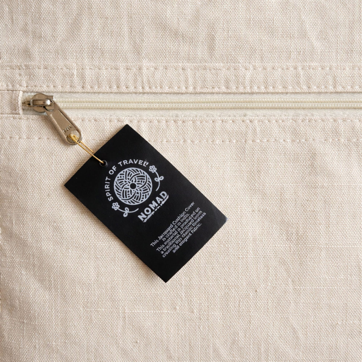 Détail de la housse de coussin Naëla en coton avec étiquette de fabrication artisanale.