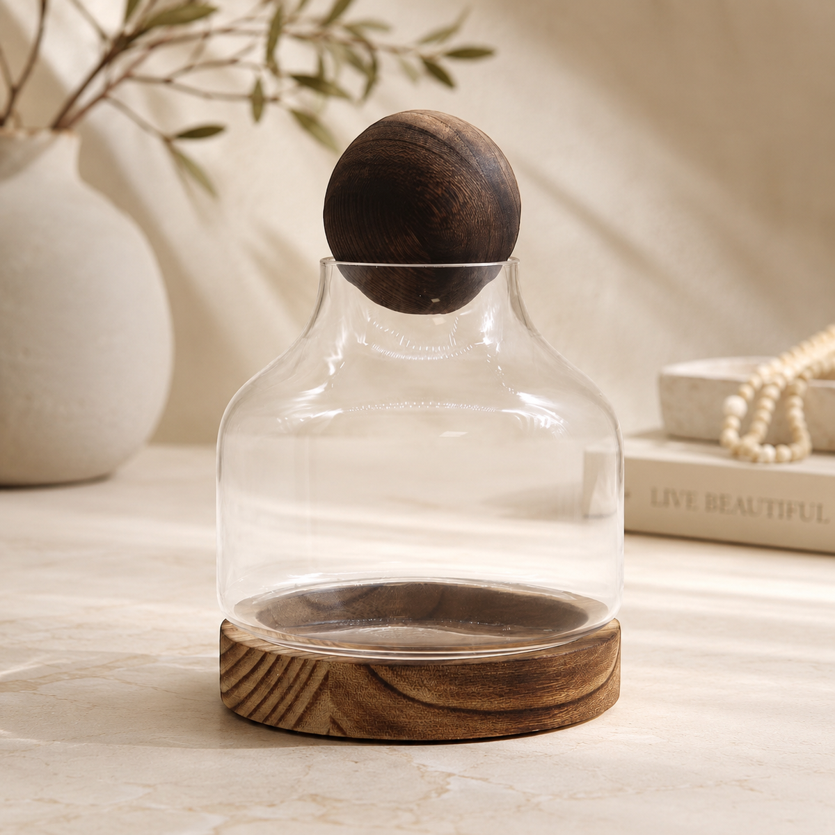 Carafe Liora Équilibre en verre transparent et bois foncé avec bouchon sphérique, posée sur une surface claire.