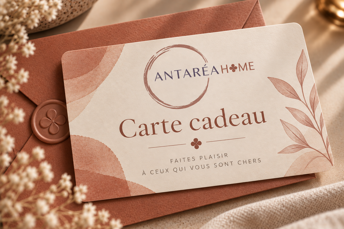 Carte cadeau Antaréa Home posée sur une enveloppe terracotta, dans une mise en scène chaleureuse et élégante aux tons beige et rose poudré.