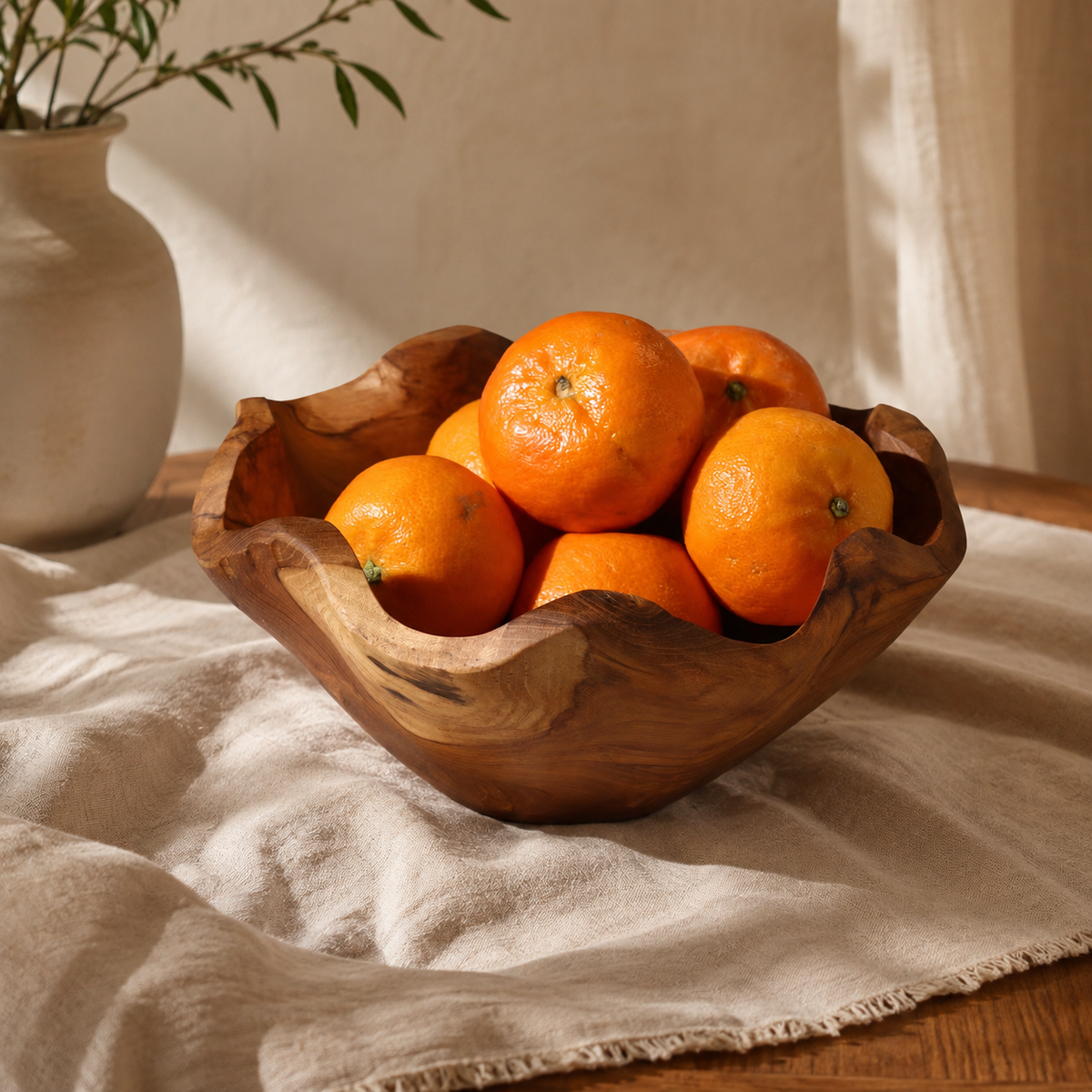Corbeille Naya en teck aux bords ondulés garnie d’oranges, posée sur un tissu clair