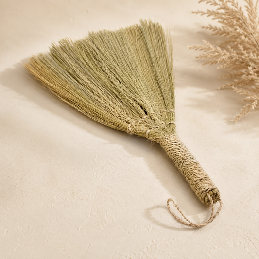 Éventail décoratif Nayra en fibres naturelles vert olive avec poignée tressée et lien de suspension.