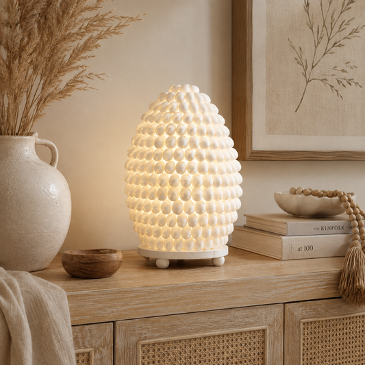 Lampe Nacréa en coquillages naturels ivoire allumée, posée sur un meuble en bois dans une ambiance bohème douce et chaleureuse.