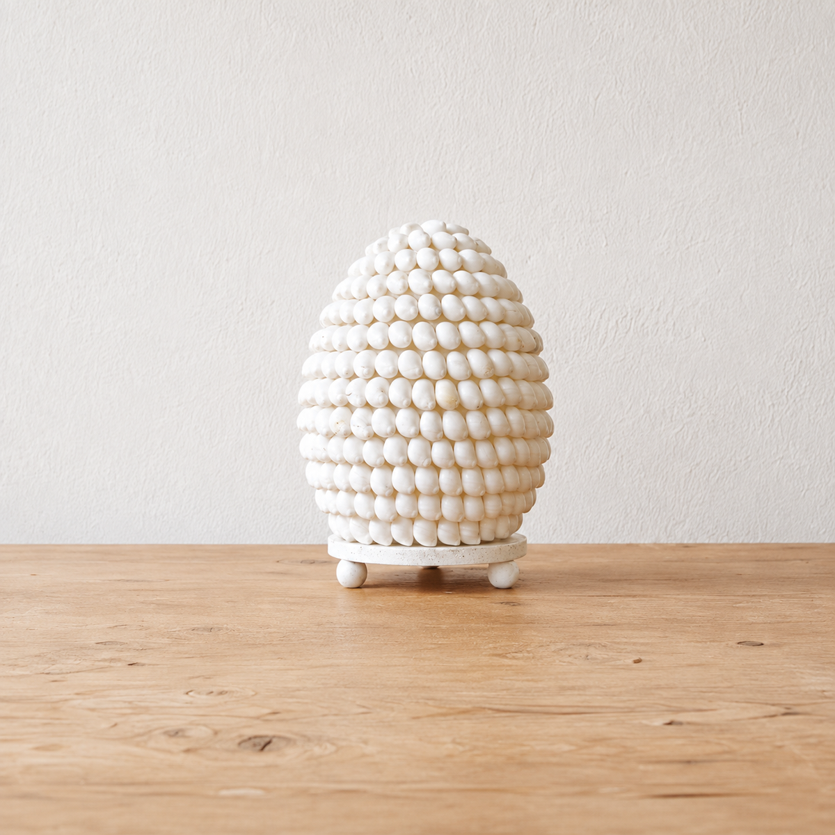 Lampe Nacréa en coquillages naturels ivoire posée sur une table en bois, avec un fond clair et épuré.