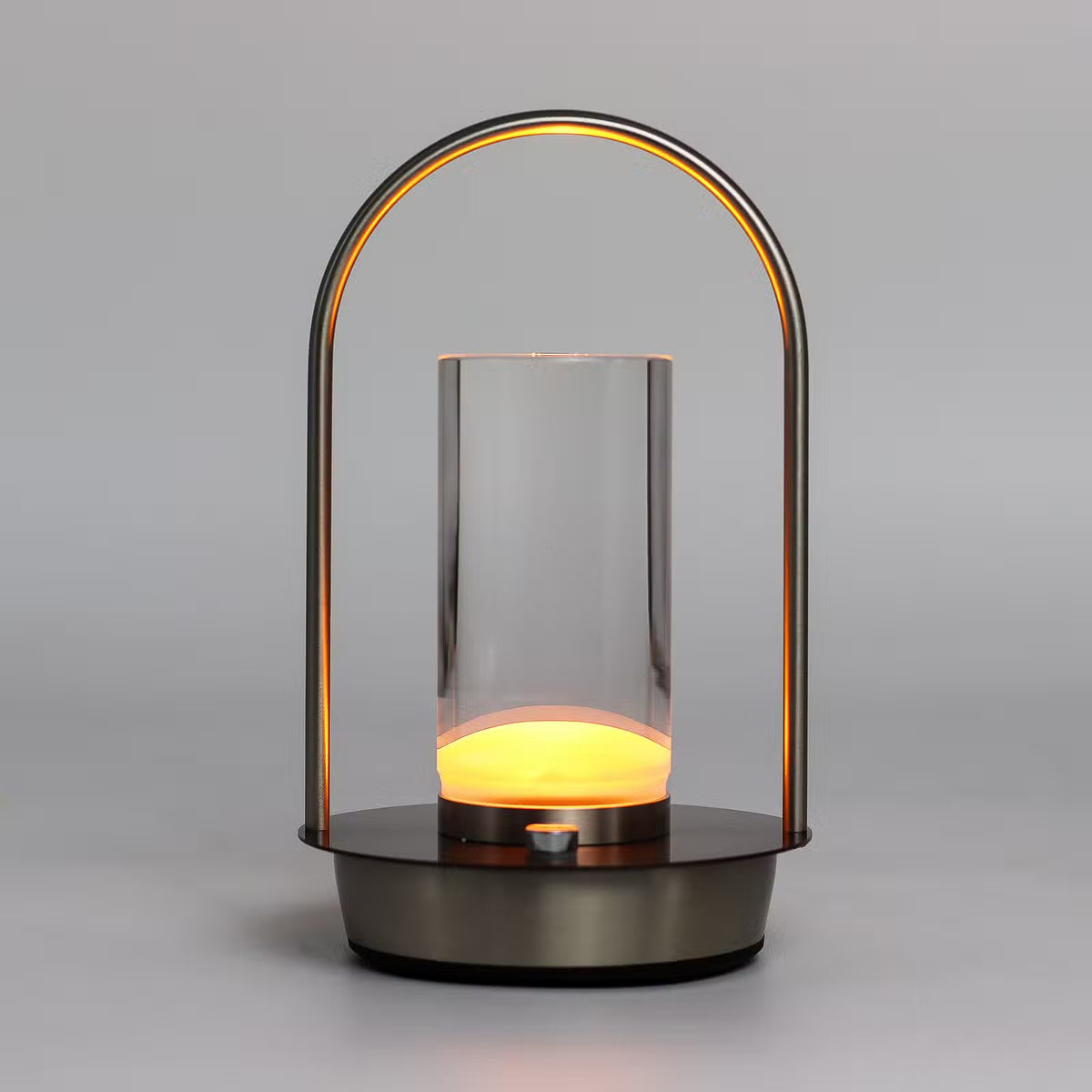 Lampe Noma Crystal allumée sur fond gris, avec lumière LED chaude diffusée à travers son cylindre transparent.
