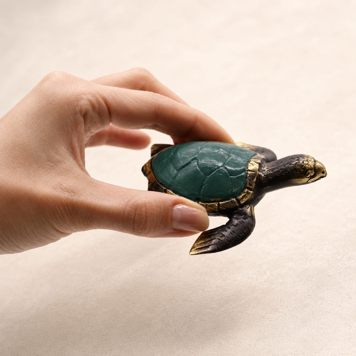 Tortue décorative Kaïa en laiton vert et doré tenue en main pour montrer l’échelle.