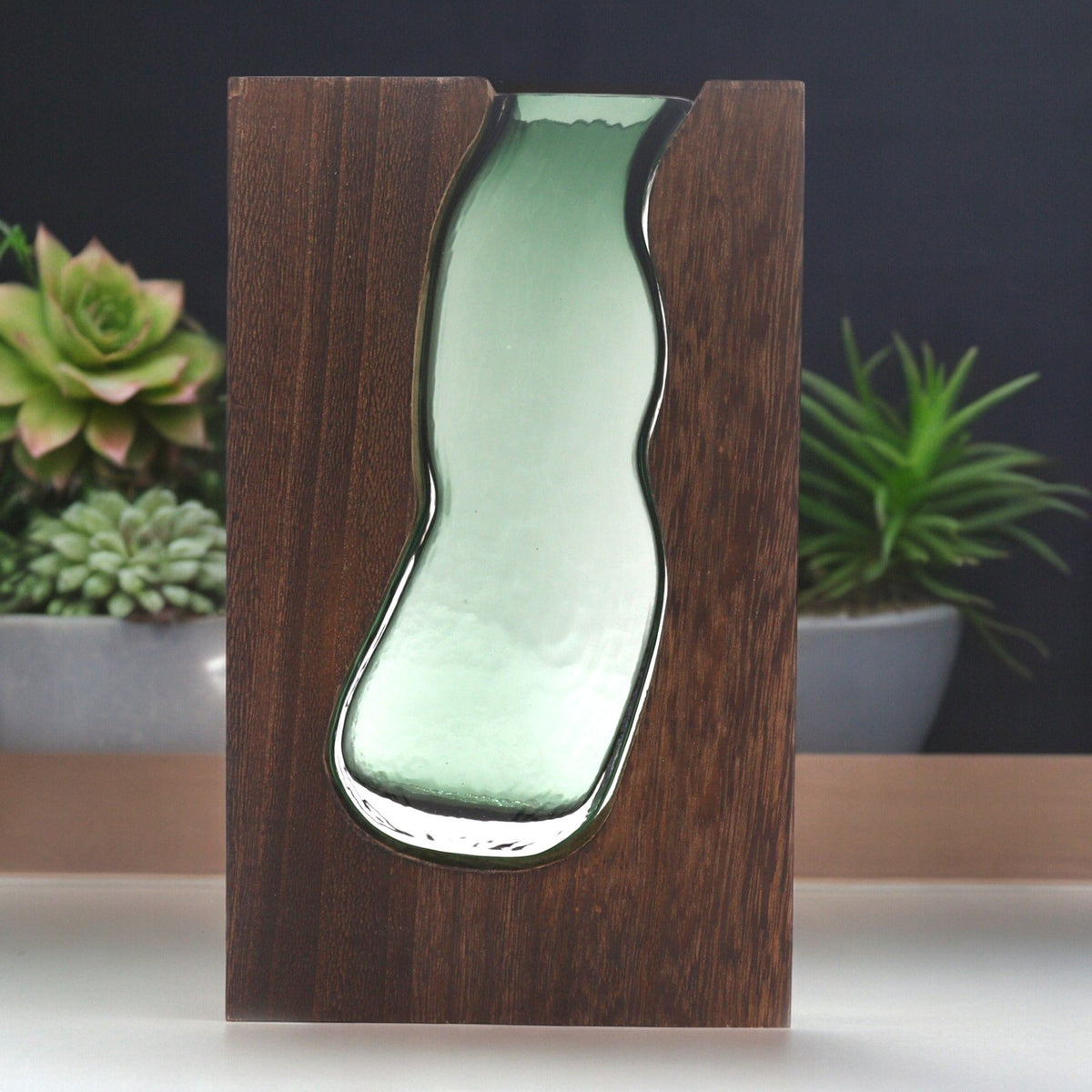 Vase décoratif Elwen 23 cm en verre aux reflets verts et bois foncé présenté avec des plantes